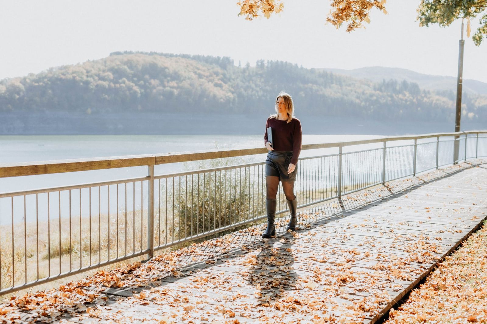 Sandra Schwalm geht an einem herbstlichen Seeufer entlang, im Hintergrund bewaldete Hügel