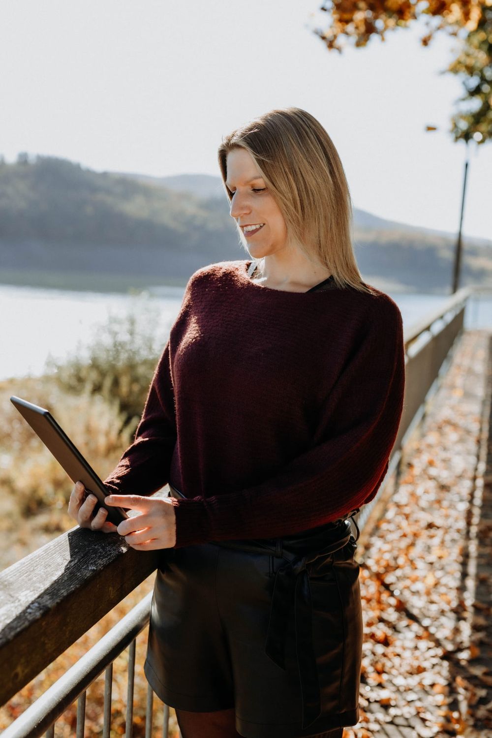 Sandra Schwalm steht an einem Seeufer und schaut lächelnd auf ein Tablet